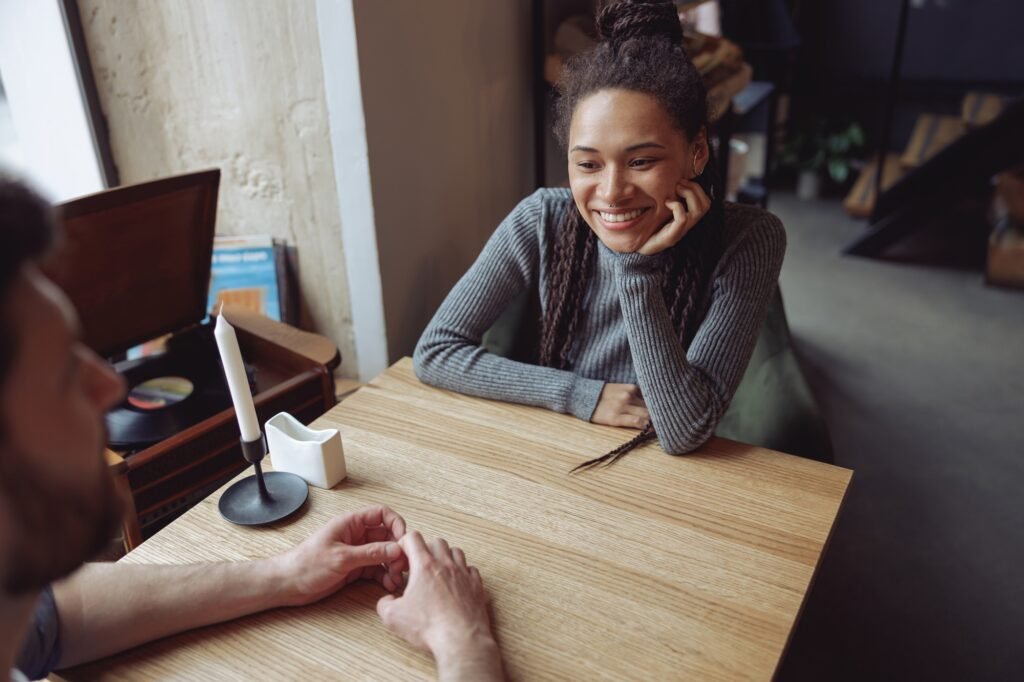 Beautiful happy young woman in love looking at man while sitting at table in cafe. Date concept.